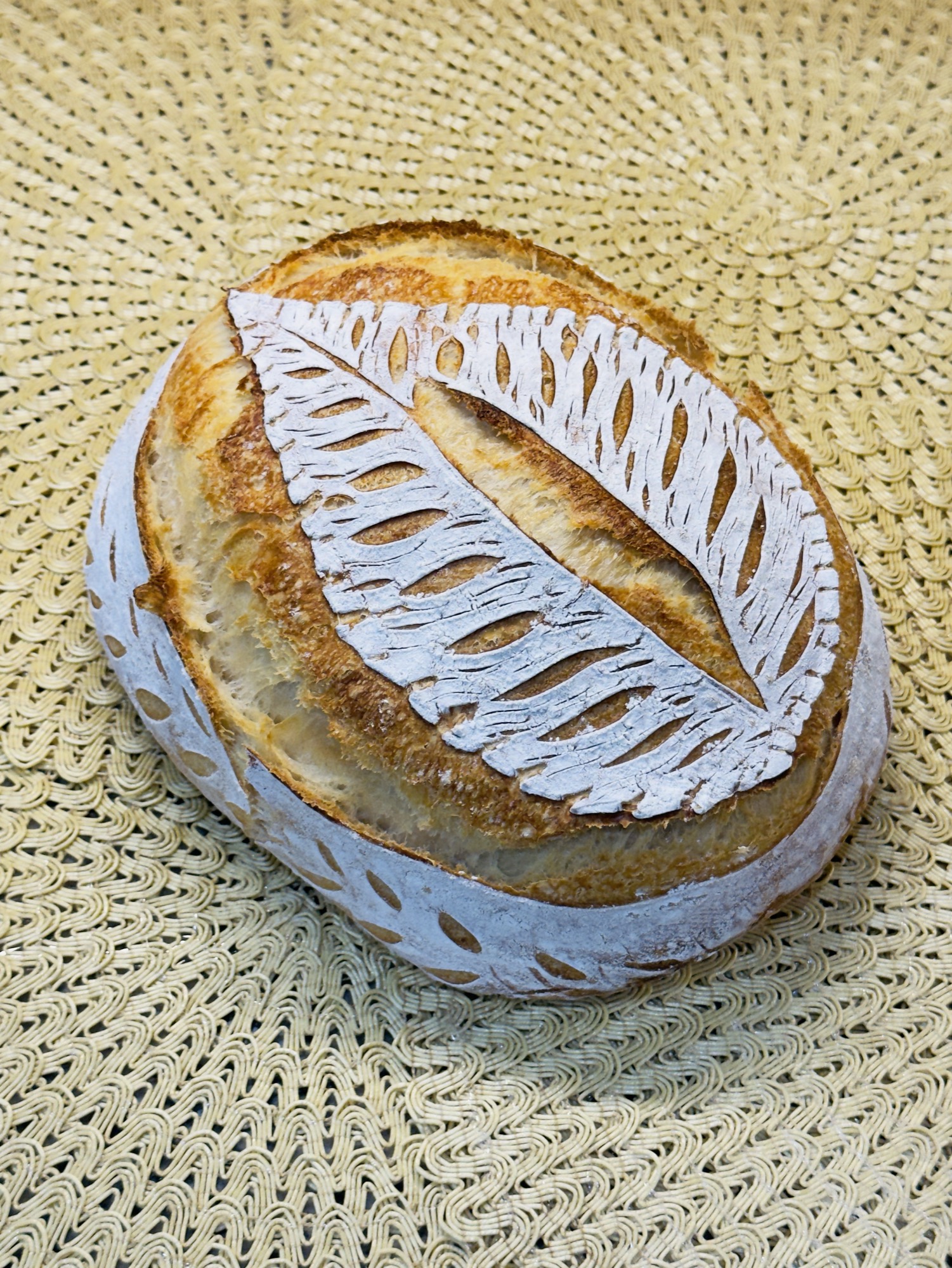 Artisan sourdough loaf with intricate fern leaf scoring on a woven mat
